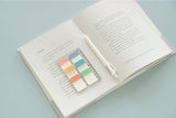 a sticky notes ruler displayed on an open book next to a white pen