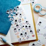 a sheet of cute astronaut deco stickers displayed on an open notebook with pens and tapes