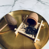 silicon pine cone shaped tea strainer displayed with some loose black tea leaves on a gold plate