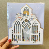 3d pop up greeting card of a white wedding church pattern with a happily ever after banner displayed on a wooden table held by a hand