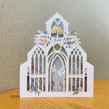 3d pop up greeting card of a white wedding church pattern with a happily ever after banner displayed on a wooden table