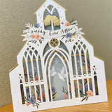 3d pop up greeting card of a white wedding church pattern with a happily ever after banner displayed on a wooden table