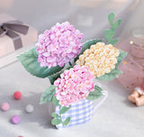 3d pop up greeting card of a bunch of hydrangea flowers in a tea cup displayed on a white desk